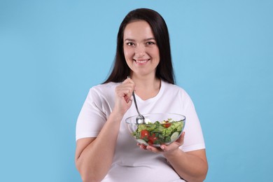 Beautiful overweight woman eating salad on light blue background. Healthy diet