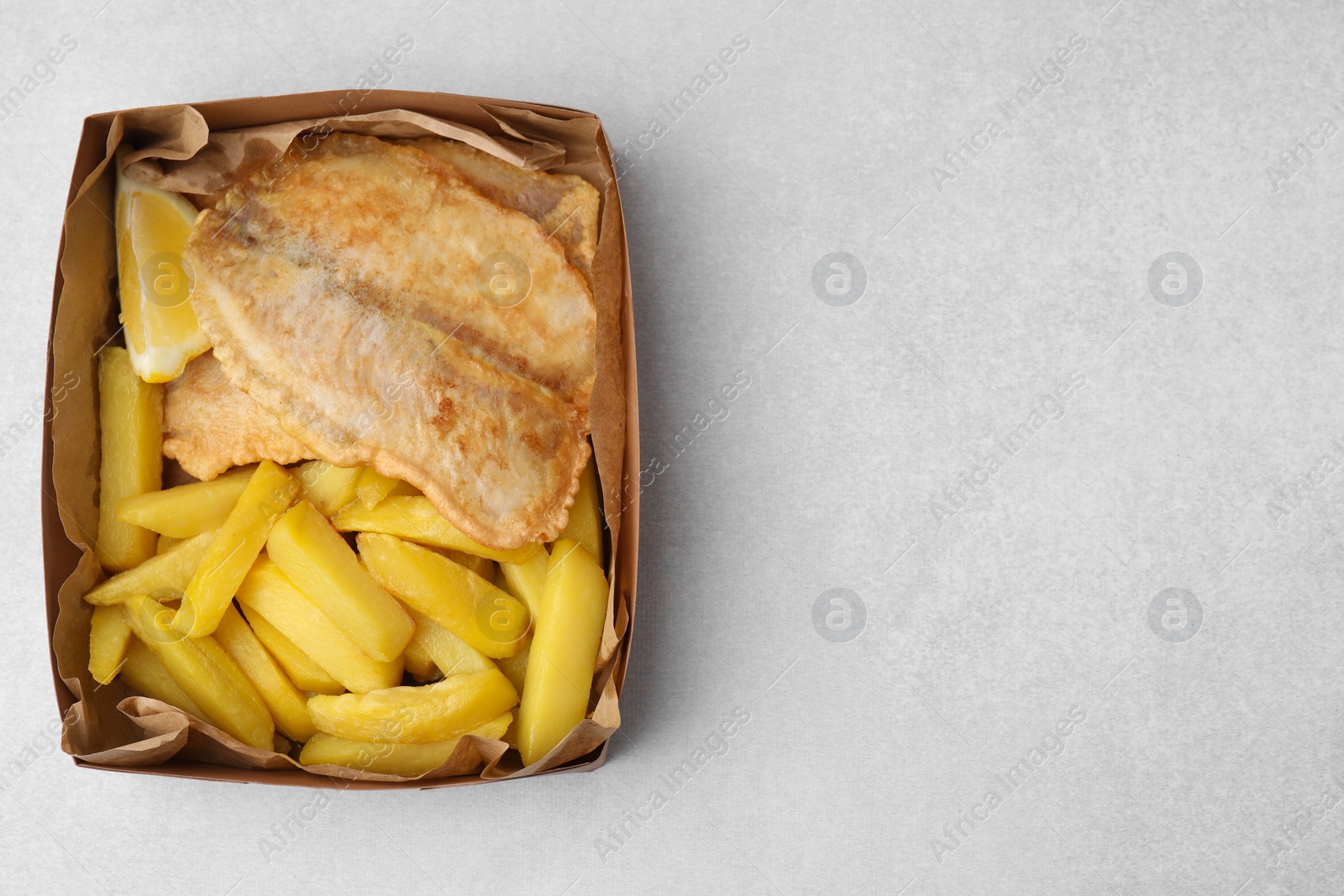 Photo of Delicious fish and chips in paper box on light gray table, top view. Space for text