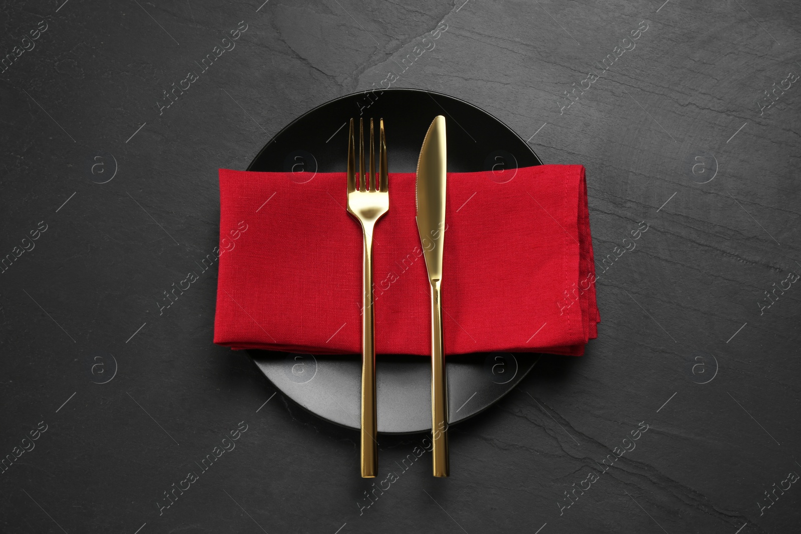 Photo of Ceramic plate, fork and knife on black table, top view