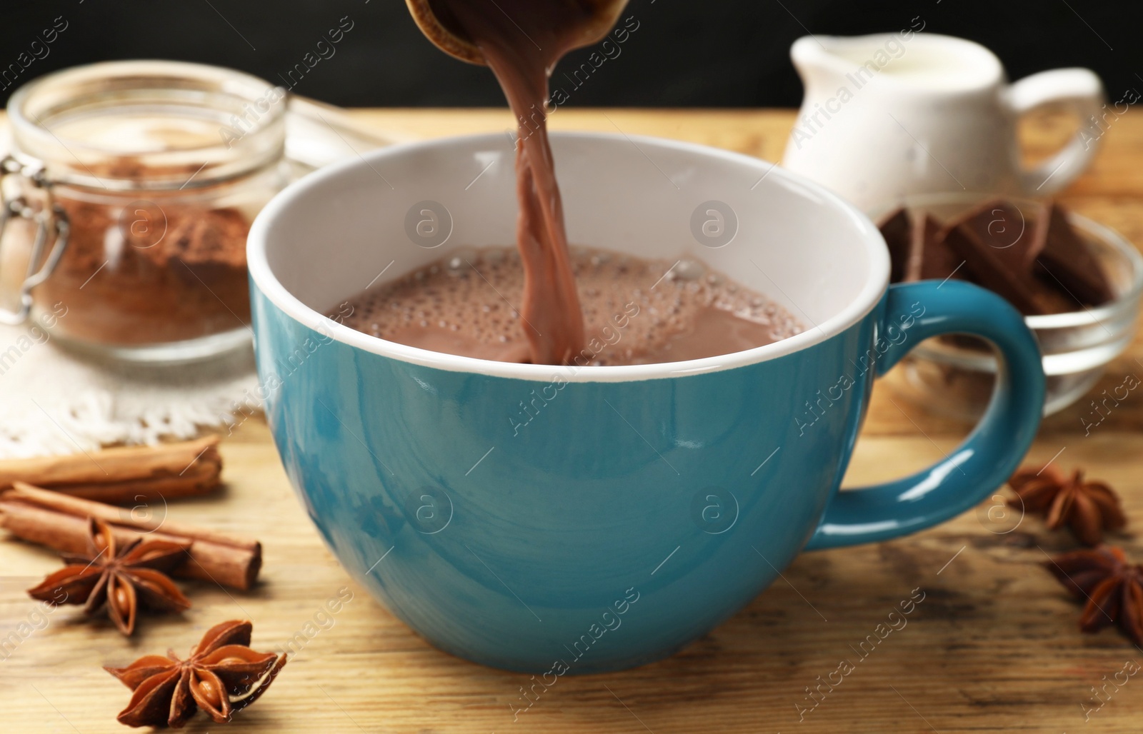 Photo of Pouring tasty hot chocolate into cup at wooden table, closeup