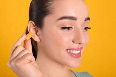 Photo of Young woman inserting foam ear plug on yellow background, closeup