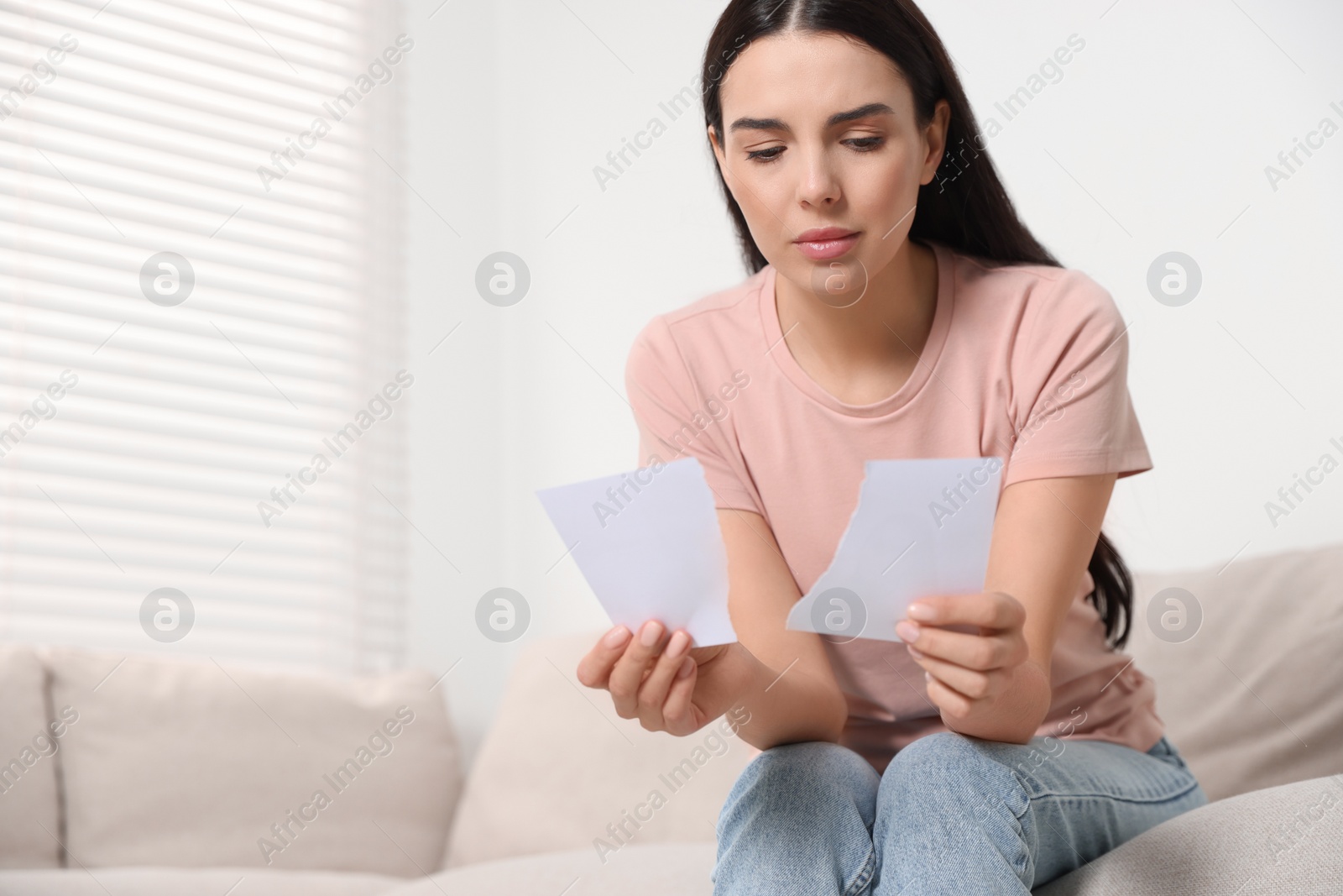 Photo of Upset woman holding parts of torn photo at home, space for text. Divorce concept