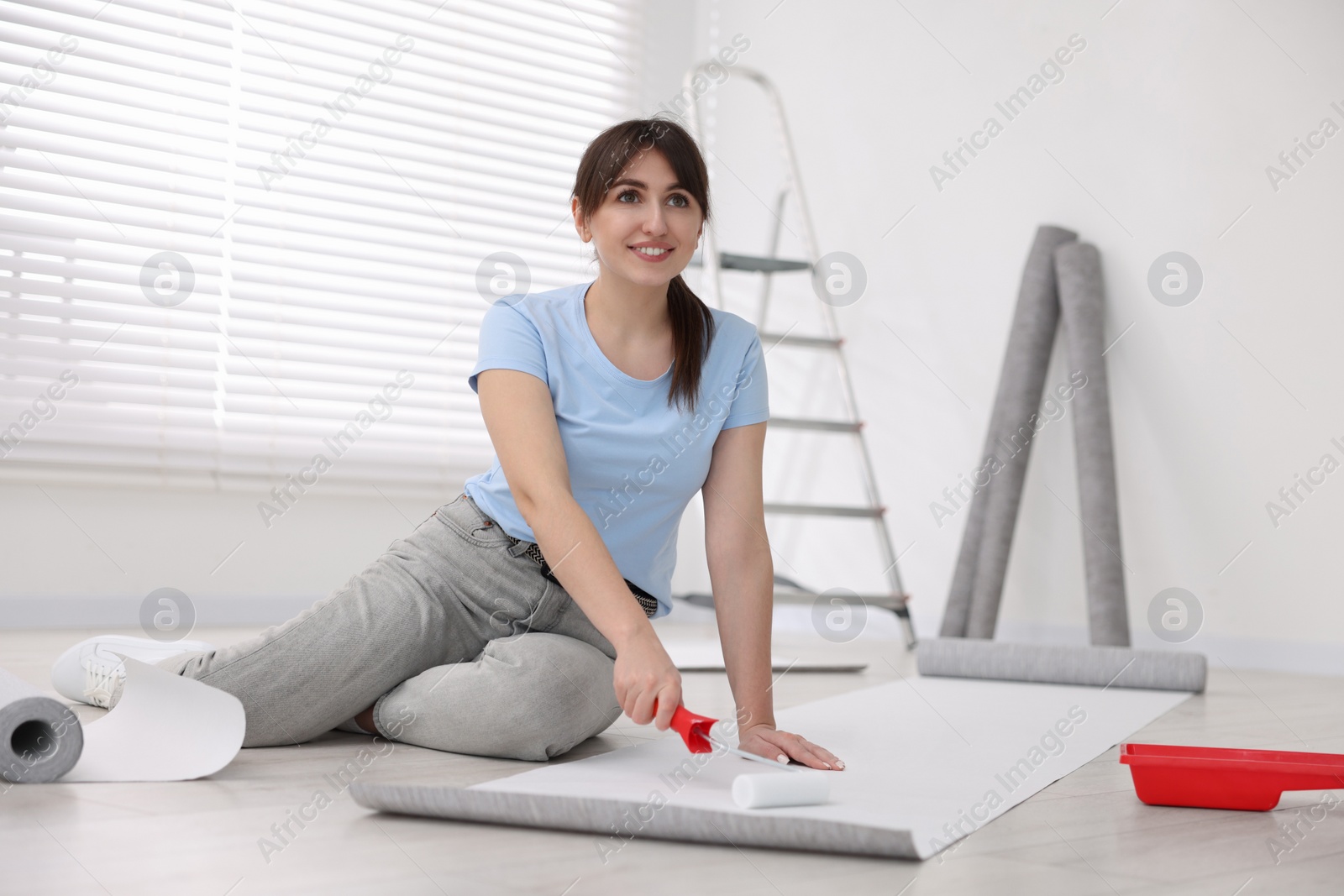 Photo of Woman applying glue onto wallpaper sheet in room