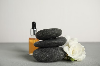 Photo of Stack of grey spa stones, flowers and oil on table