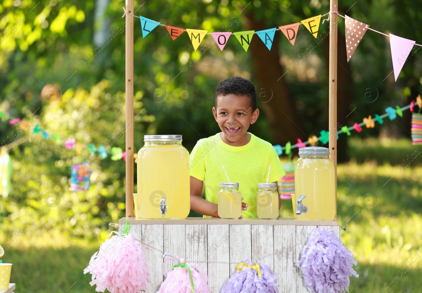 Photo of Cute little African-American boy at lemonade stand in park. Summer refreshing natural drink