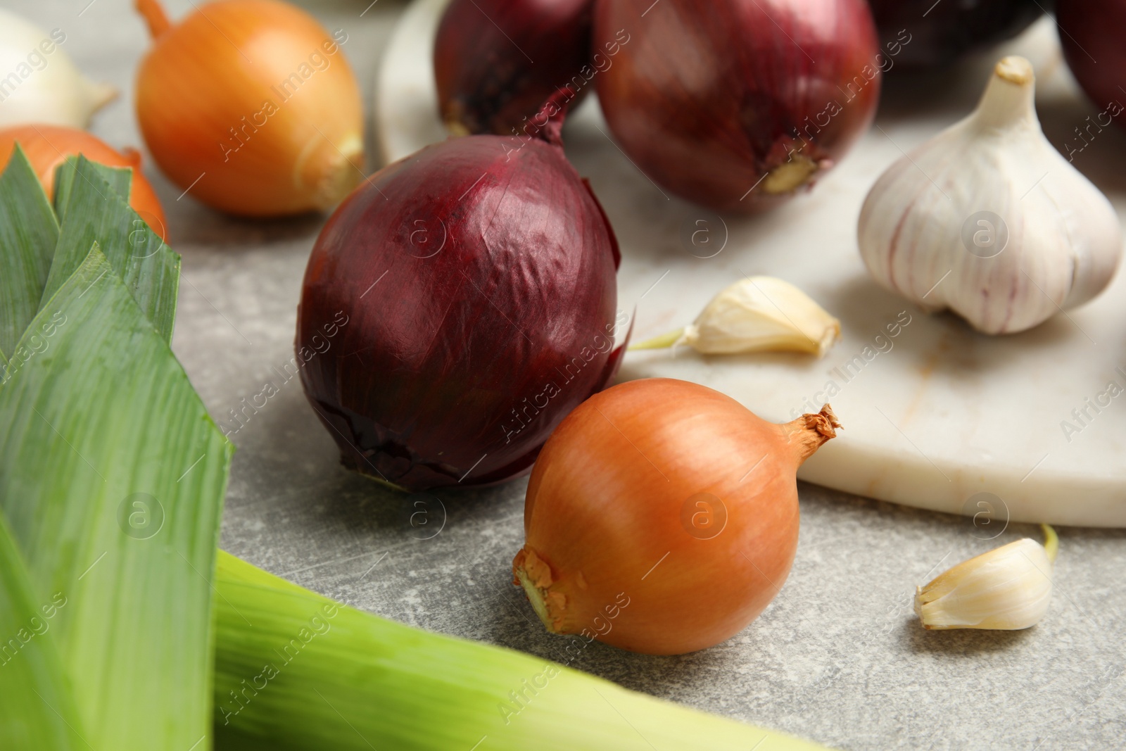 Photo of Fresh onion bulbs, leeks and garlic on grey table, closeup