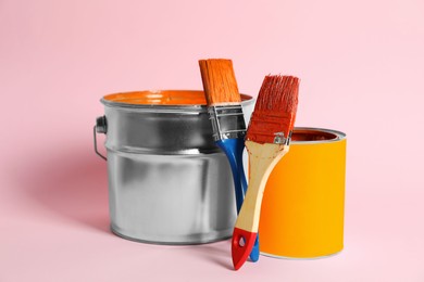 Bucket of orange paint, can and brushes on pink background