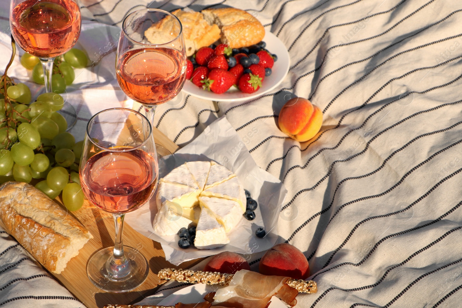 Photo of Glasses of delicious rose wine and food on white picnic blanket