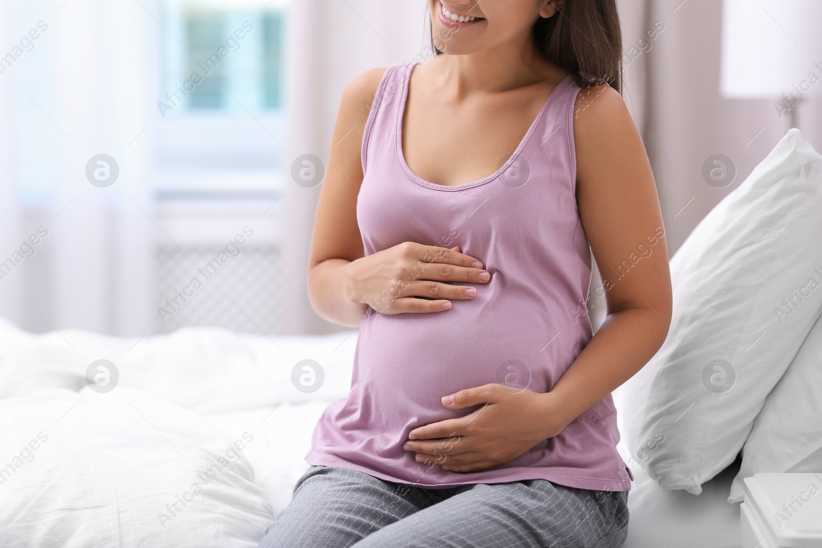 Photo of Happy pregnant woman sitting on bed at home, closeup