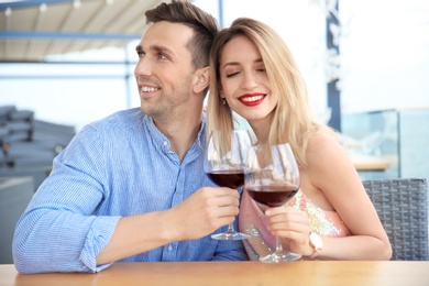 Photo of Young romantic couple with glasses of red wine at table