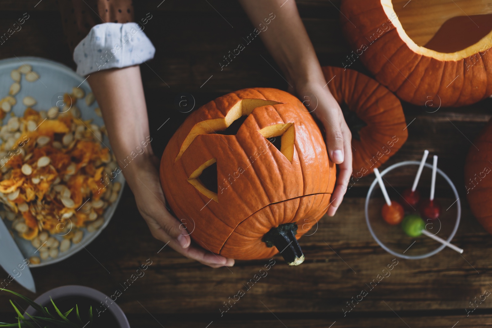 Photo of Woman with pumpkin jack o'lantern at wooden table, top view. Halloween celebration