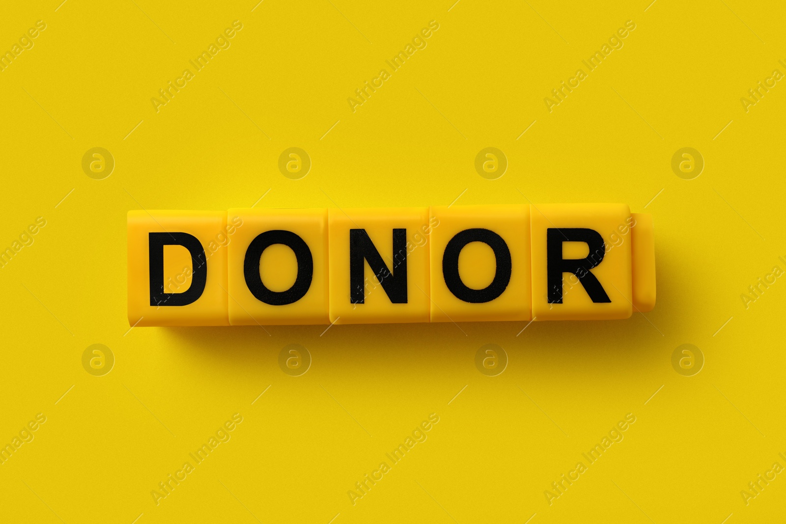 Photo of Word Donor made of cubes on yellow background, top view