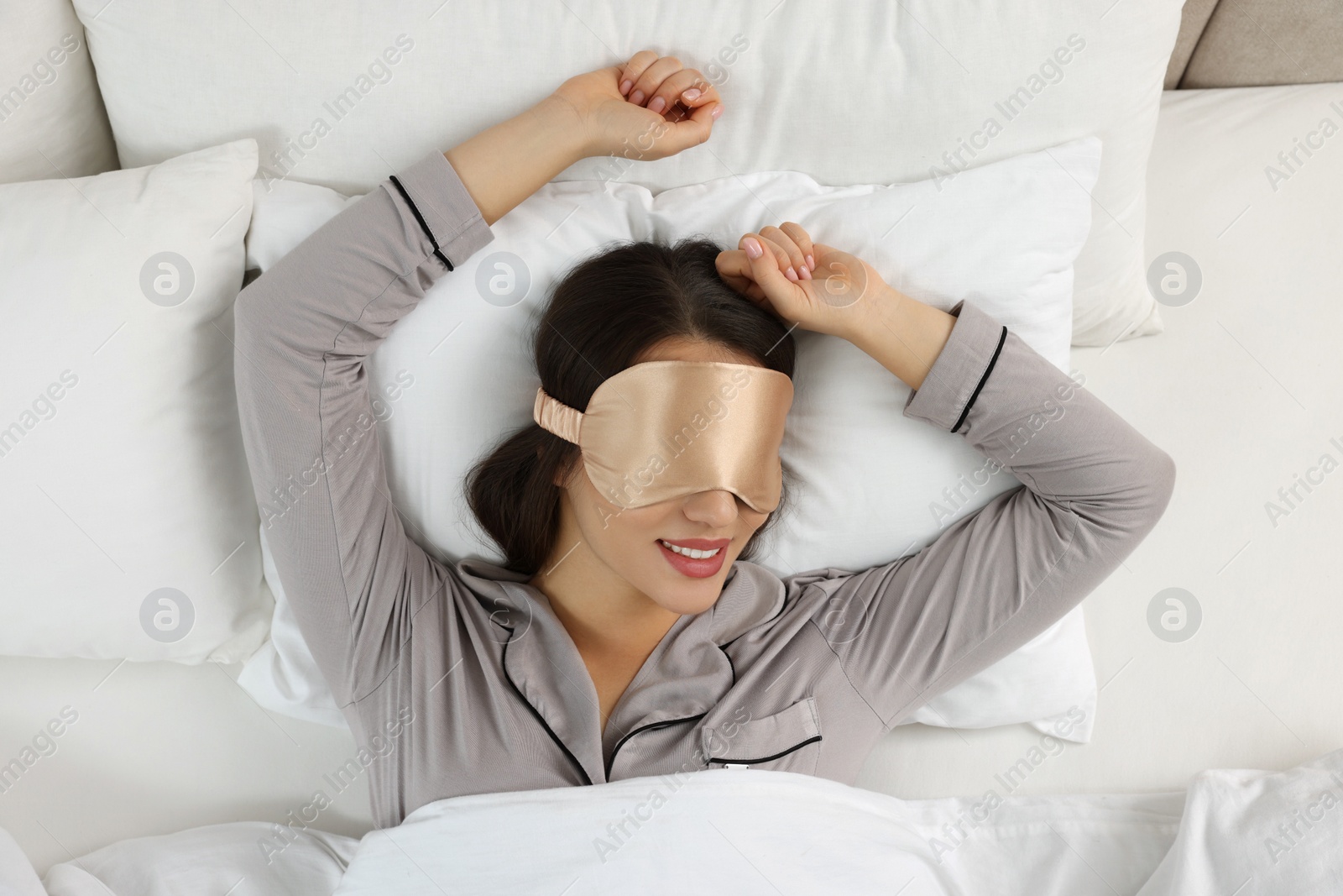 Photo of Young woman with sleeping mask in bed, top view