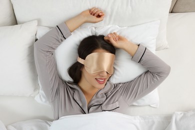 Young woman with sleeping mask in bed, top view
