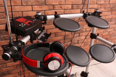 Photo of Modern electronic drum kit with headphones near red brick wall indoors. Musical instrument