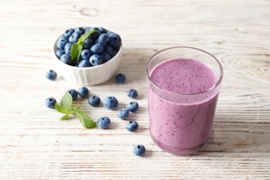 Tasty blueberry smoothie in glass and bowl with fresh berries on table