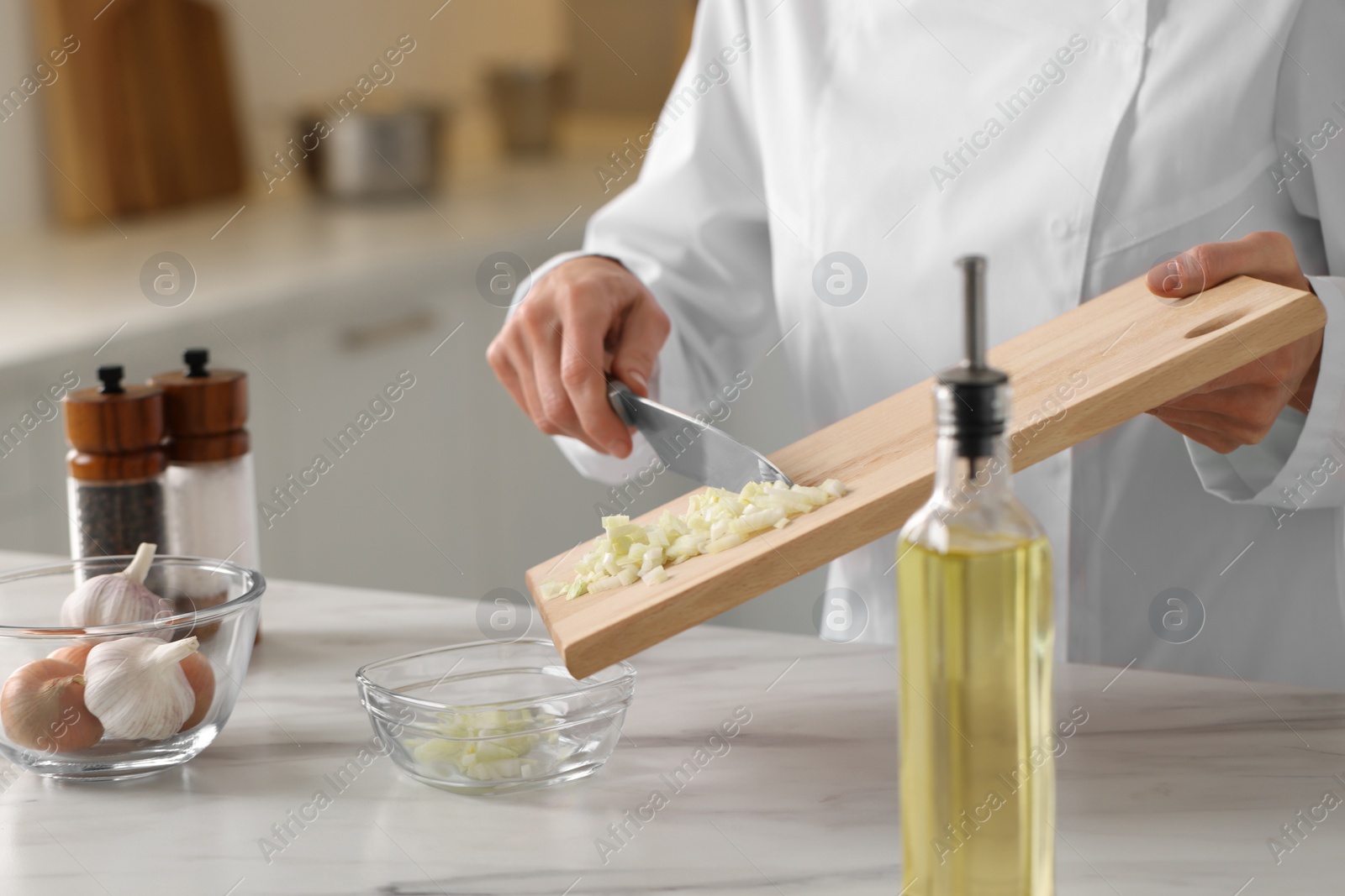 Photo of Professional chef putting cut onion into bowl at white marble table indoors, closeup