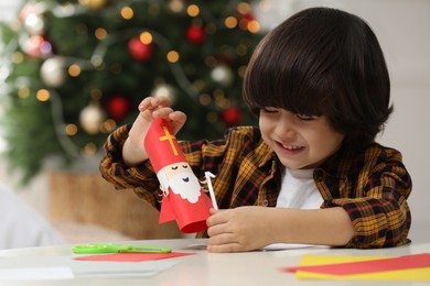 Photo of Cute little boy making paper Saint Nicholas toy at home