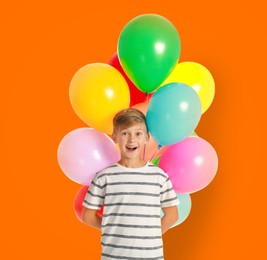 Image of Happy little boy holding bunch of colorful balloons on orange background