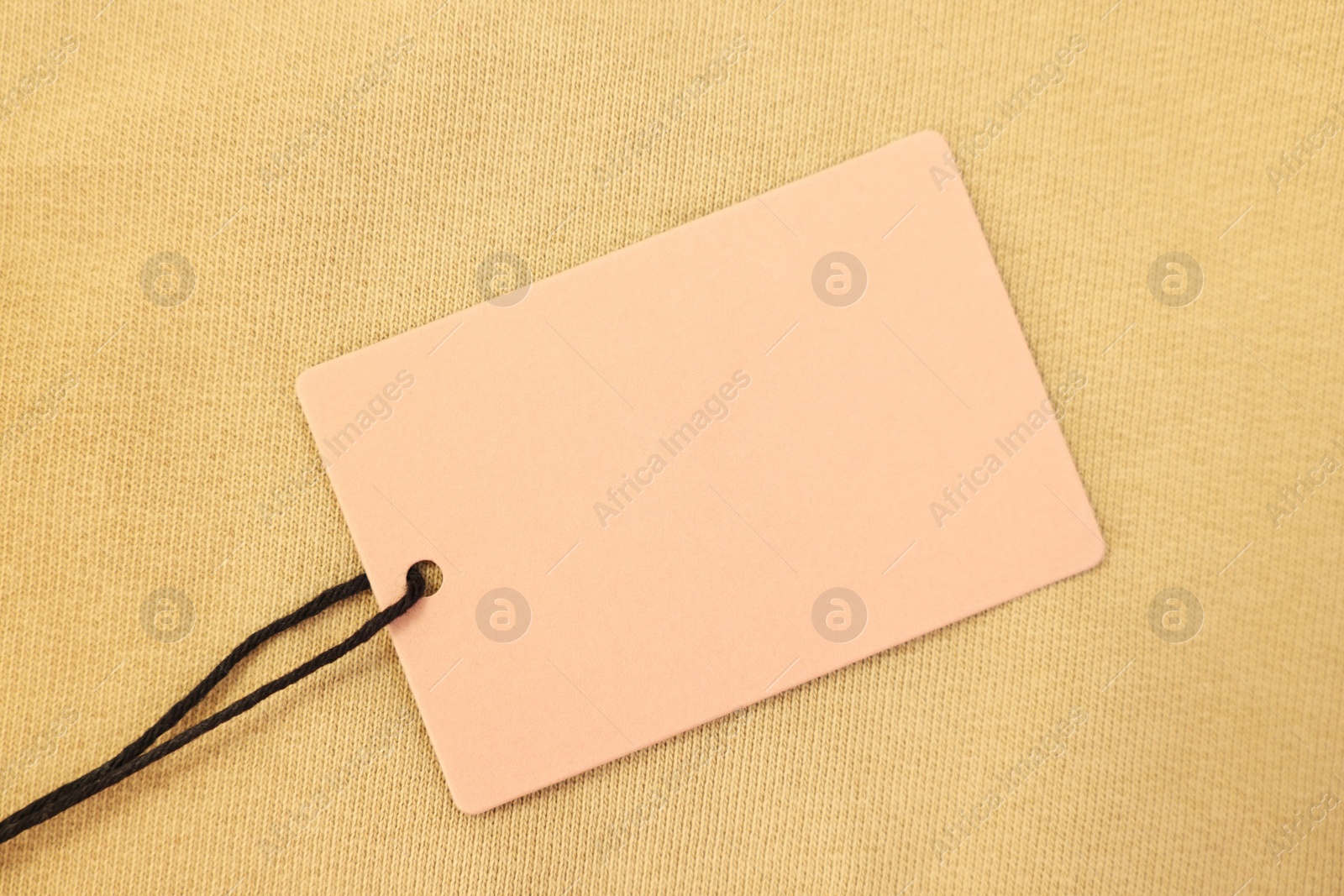 Photo of Cardboard tag on beige garment, top view. Space for text