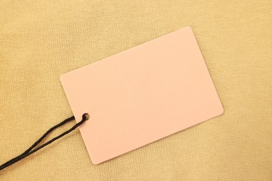 Photo of Cardboard tag on beige garment, top view. Space for text