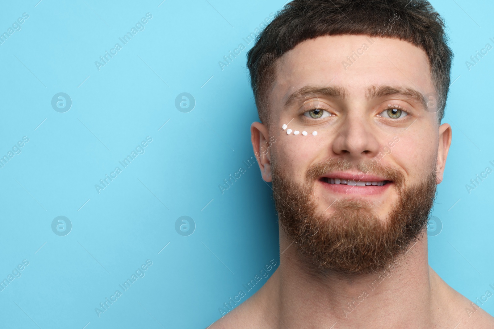 Photo of Handsome man with moisturizing cream on his face against light blue background, space for text