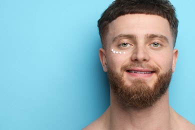 Handsome man with moisturizing cream on his face against light blue background, space for text