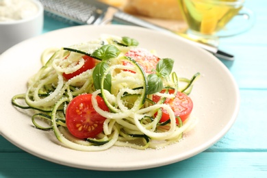 Photo of Delicious zucchini pasta with cherry tomatoes, basil and grated cheese served on light blue wooden table, closeup