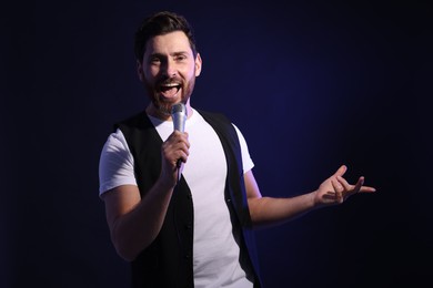 Photo of Handsome man with microphone singing on dark blue background