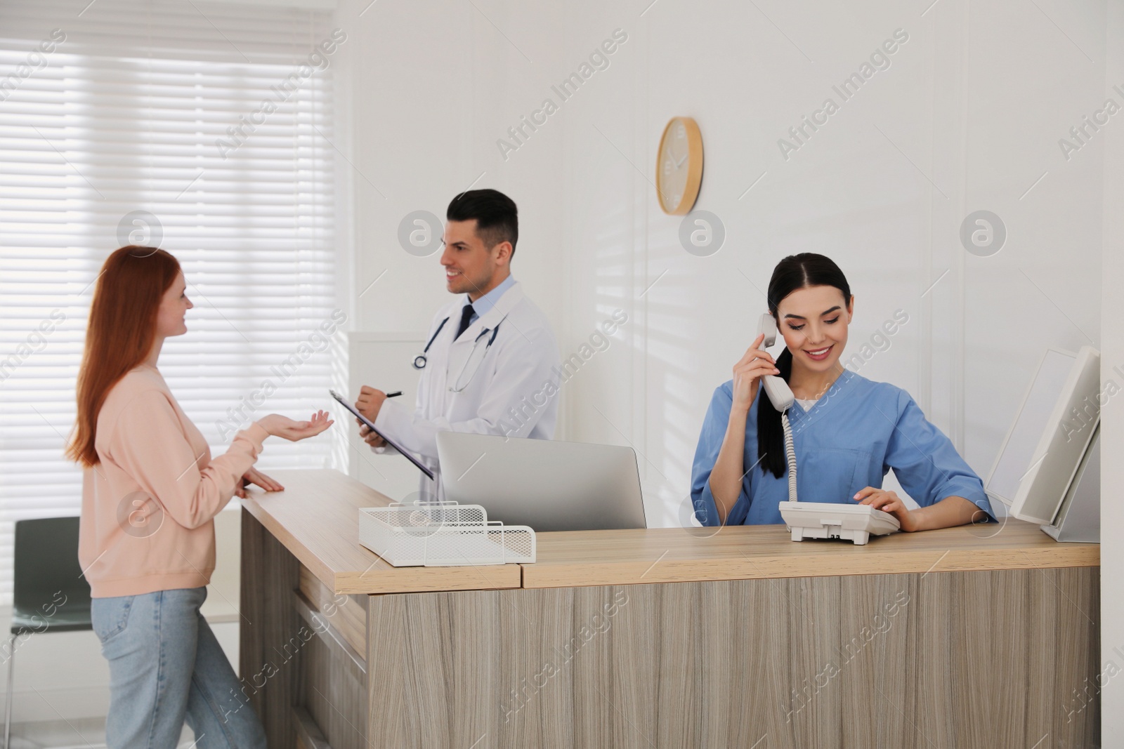 Photo of Receptionist talking on phone while doctor working with patient in hospital