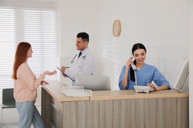 Photo of Receptionist talking on phone while doctor working with patient in hospital