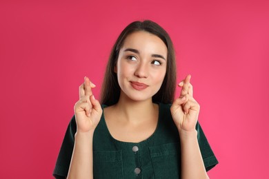 Photo of Woman with crossed fingers on pink background. Superstition concept