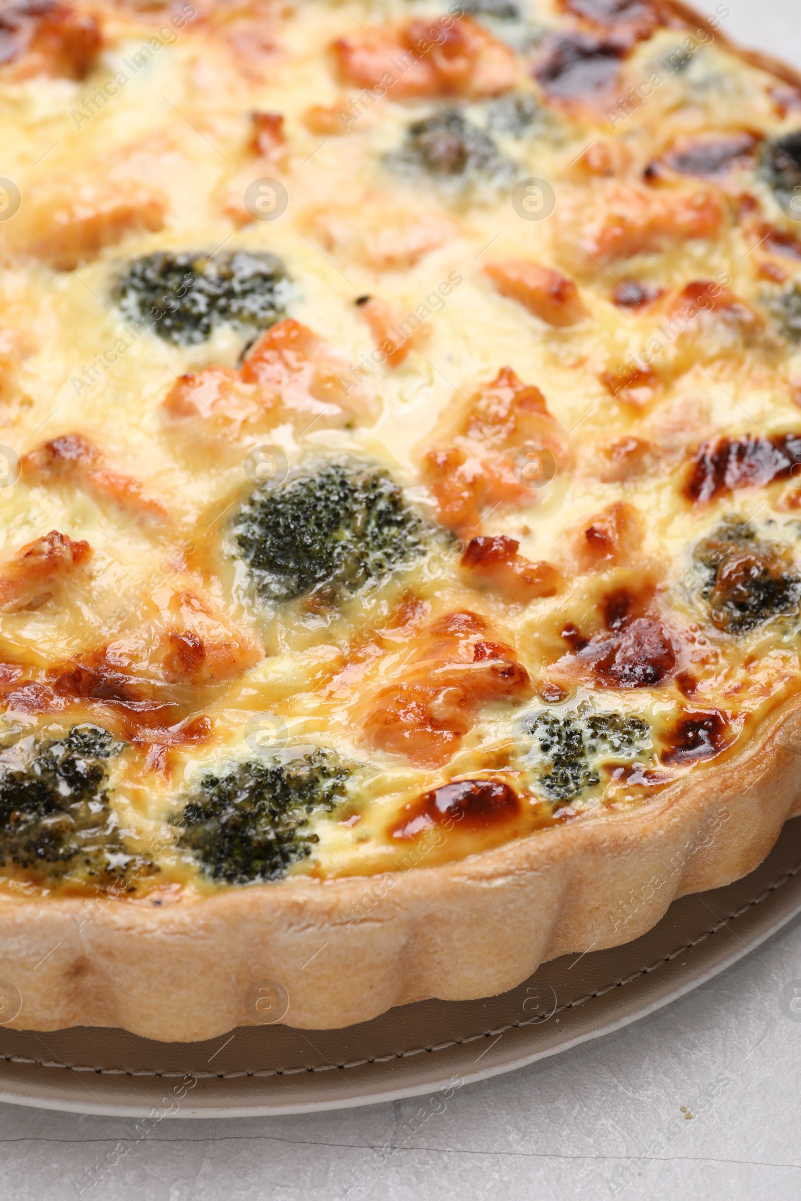 Photo of Delicious homemade quiche with salmon and broccoli on light gray table, closeup