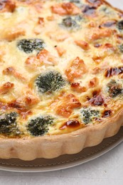 Delicious homemade quiche with salmon and broccoli on light gray table, closeup