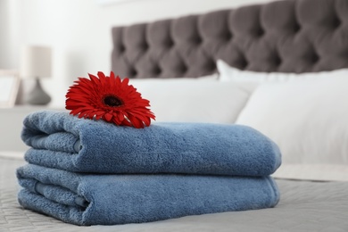 Stack of clean towels with flower on bed indoors