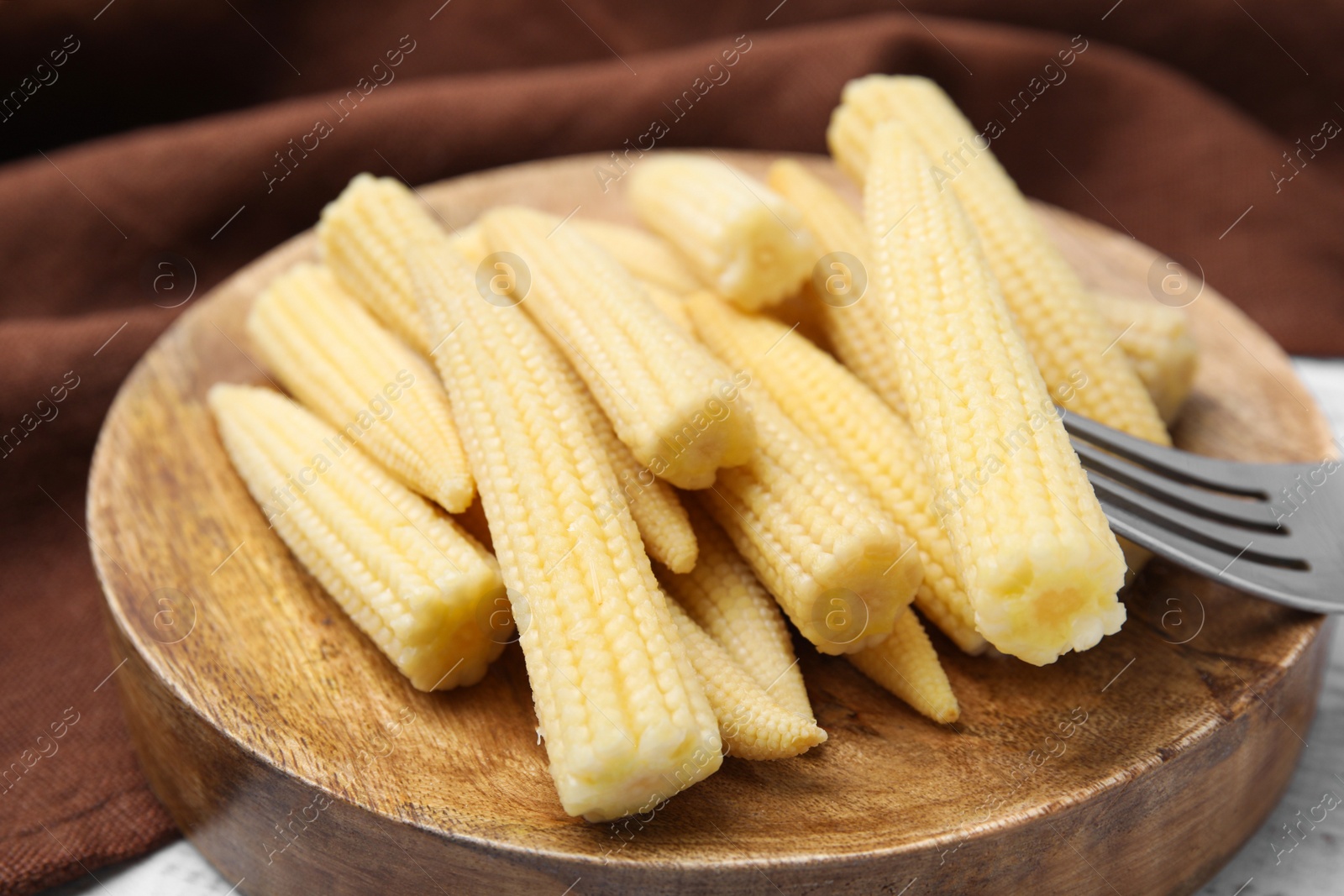 Photo of Pickled baby corn and fork on white wooden table, closeup