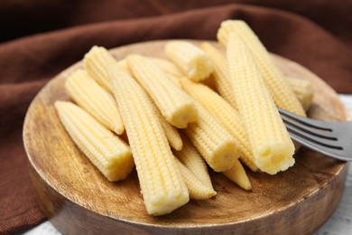 Photo of Pickled baby corn and fork on white wooden table, closeup