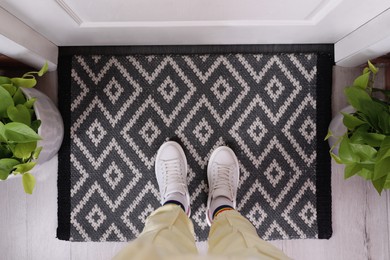 Photo of Woman wearing stylish sneakers on door mat in hall, top view