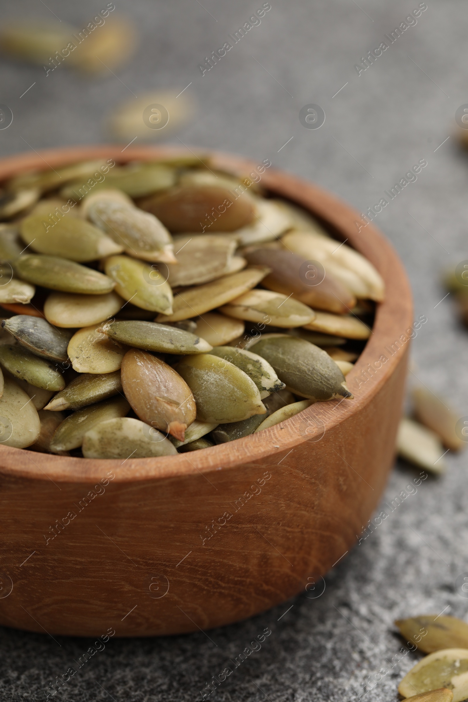 Photo of Wooden bowl with peeled pumpkin seeds on grey table, closeup