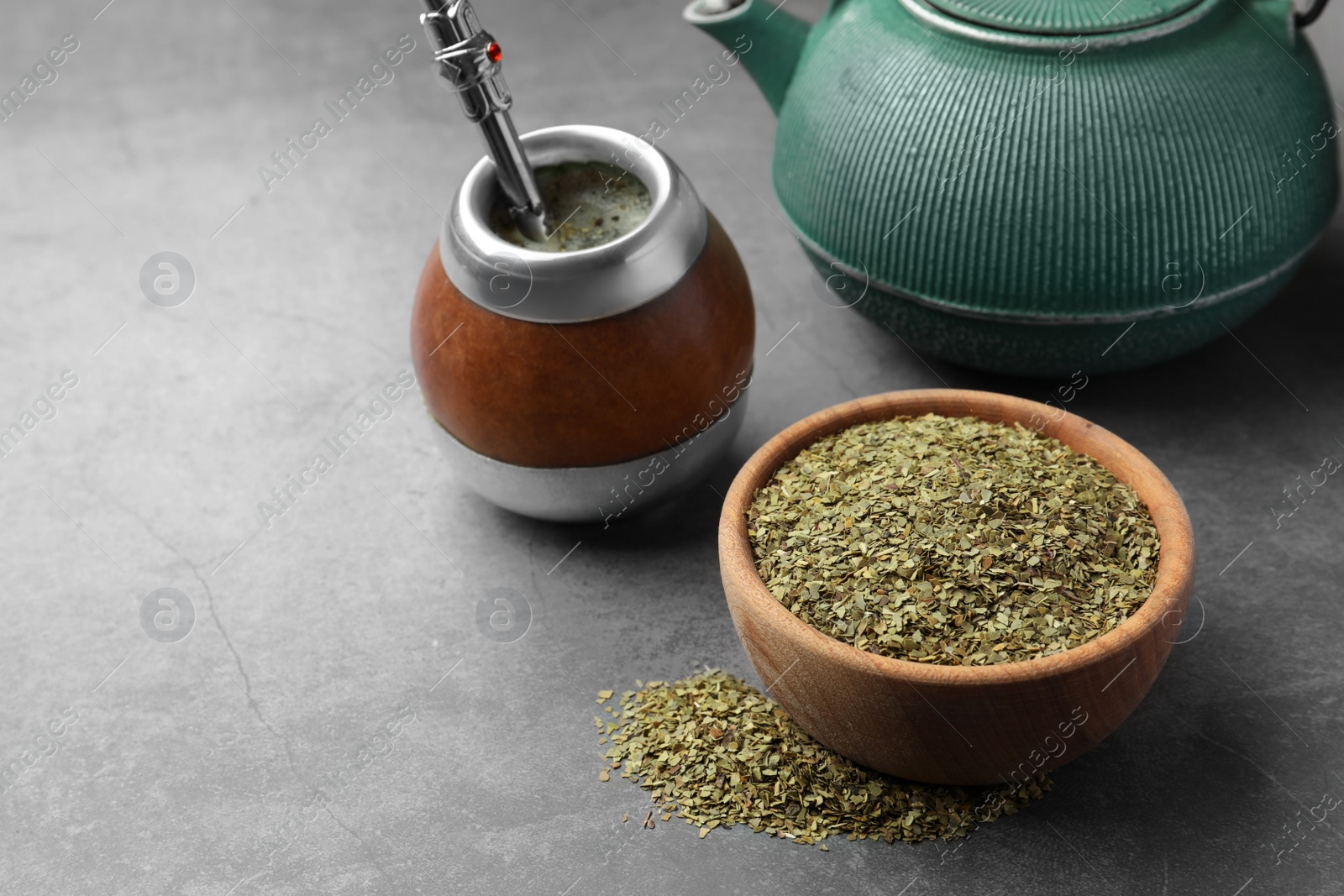 Photo of Calabash with bombilla, teapot and bowl of mate tea leaves on grey table, space for text