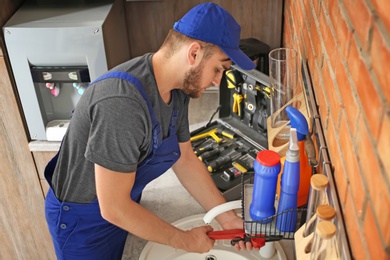 Photo of Professional plumber in uniform fixing kitchen sink