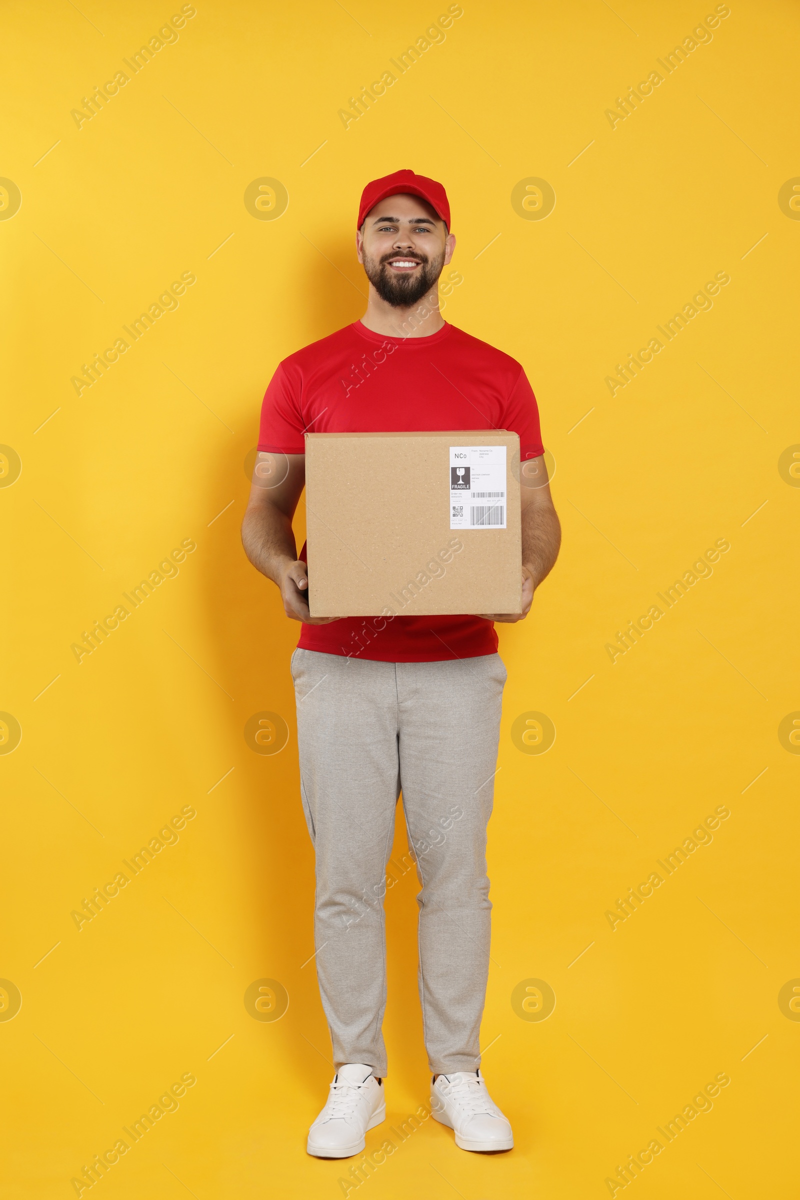 Photo of Courier holding cardboard box on yellow background