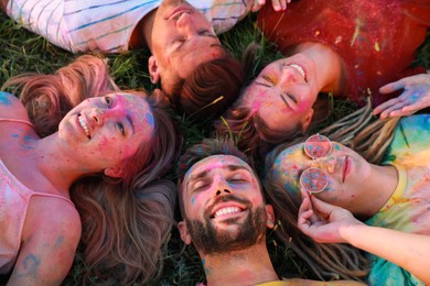 Happy friends covered with colorful powder dyes on green grass outdoors. Holi festival celebration