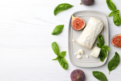 Photo of Delicious goat cheese with figs and basil on white wooden table, flat lay. Space for text