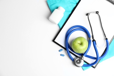 Flat lay composition with stethoscope, apple and clipboard on light background. Medical equipment