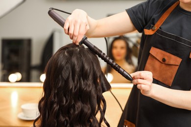 Hair styling. Hairdresser curling woman's hair in salon, closeup