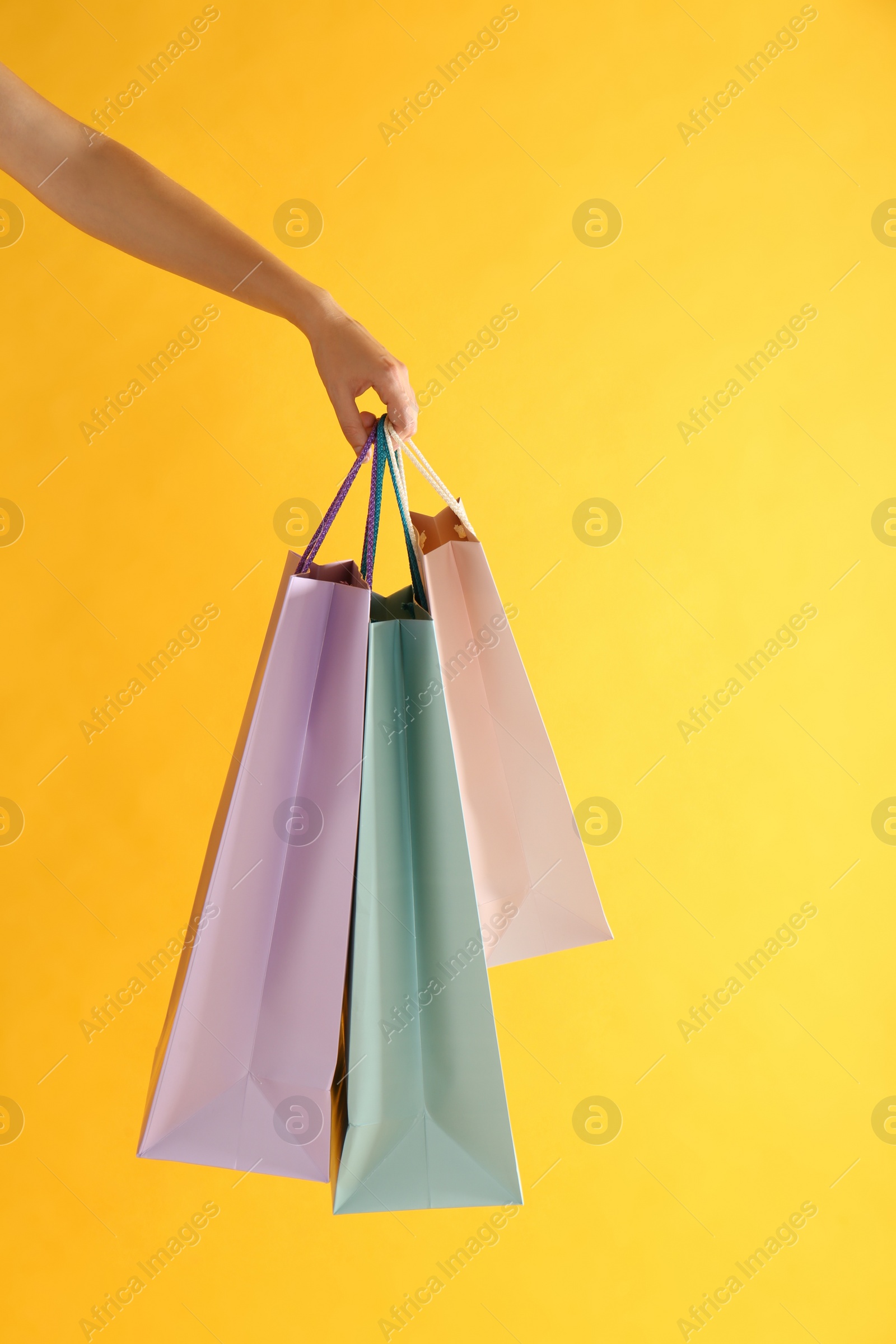 Photo of Woman with paper shopping bags on yellow background, closeup