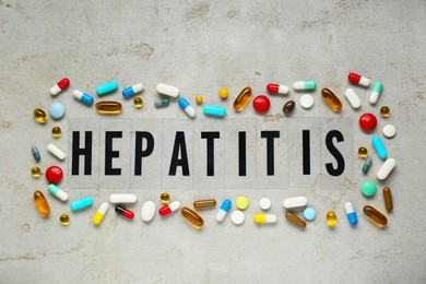 Photo of Word Hepatitis and pills on light grey table, flat lay