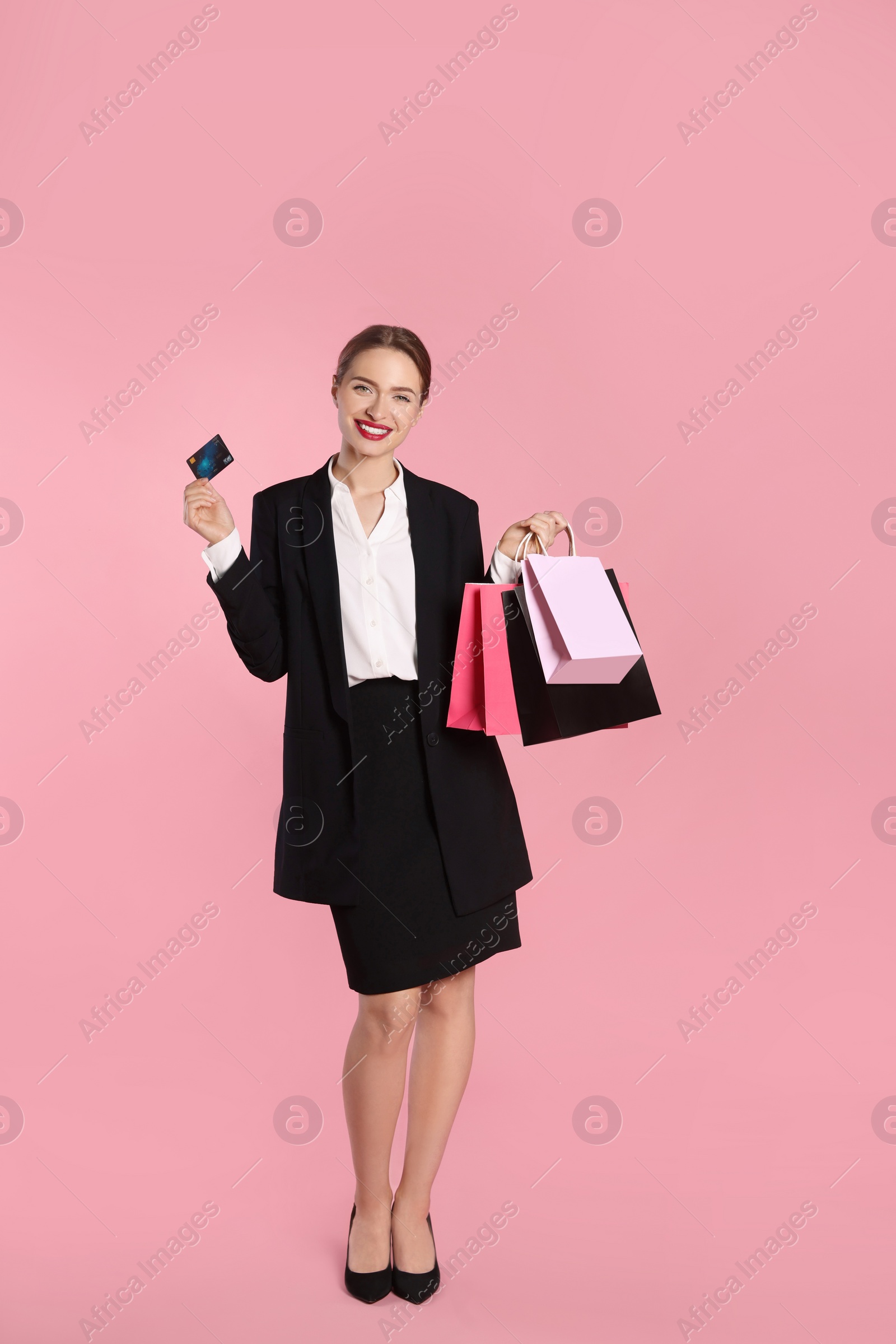 Photo of Happy young woman with shopping bags and credit card on light pink background. Big sale