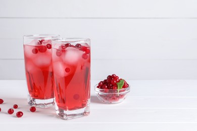 Photo of Tasty cranberry juice with ice cubes in glasses and fresh berries on white wooden table. Space for text